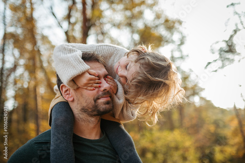 Father walking with daughter on his shoulders across autumn forest. Dad and girl having fun outdoors.