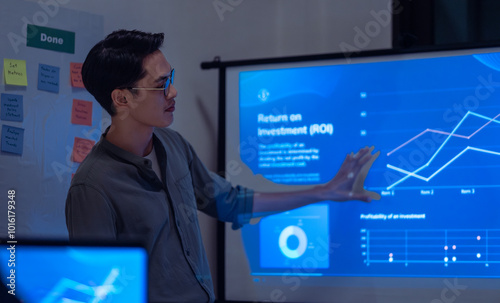 asian leader present business presentation in a dimly lit office, analyzing financial charts and data projections on a screen