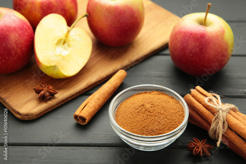 Red apple, cinnamon sticks and cinnamon in bowl on black wooden background.