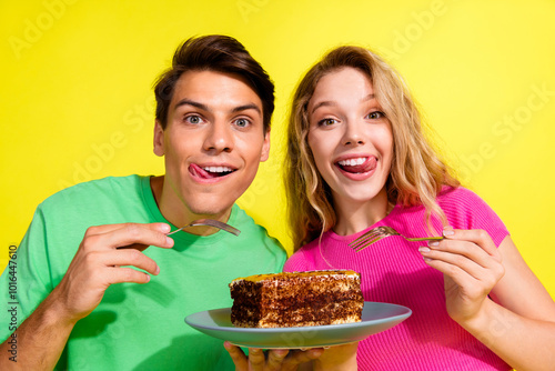 Photo of two nice young people eat large piece cake wear t-shirt isolated on bright yellow color background