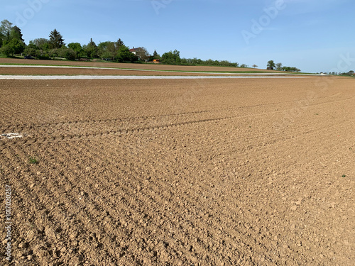 A wide-open agricultural field with freshly plowed soil, ready for planting under a bright blue sky.