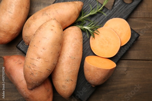 Fresh raw sweet potatoes and rosemary on wooden table, top view