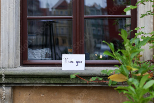 A white card with a handwritten inscription "thank you" on an old, decorative window sill