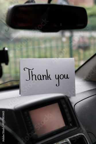 A white card with a handwritten inscription "thank you" on the dashboard of a car