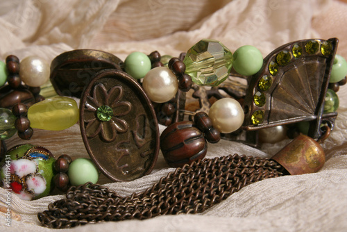 Still life fragment of costume jewellery bracelets with floral details in green on beige rough fabric