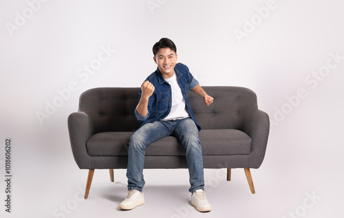 Full body image of young Asian man posing on sofa on white background