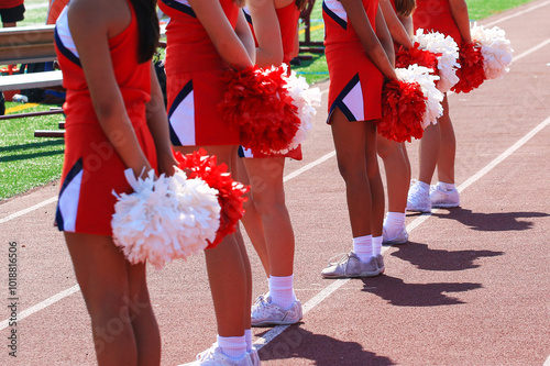 Cheerleaders holding their pom poms behind their backs on the sidelines of a football game