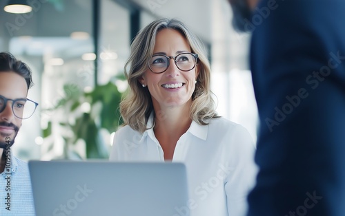 A woman smiles at colleagues in a modern office setting, showcasing collaboration and positivity in a professional environment.