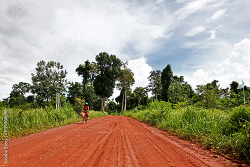 Phnom Kulen, Cambodia - September 13, 2013: A female resident on a bicycle is passing by on red dirt road