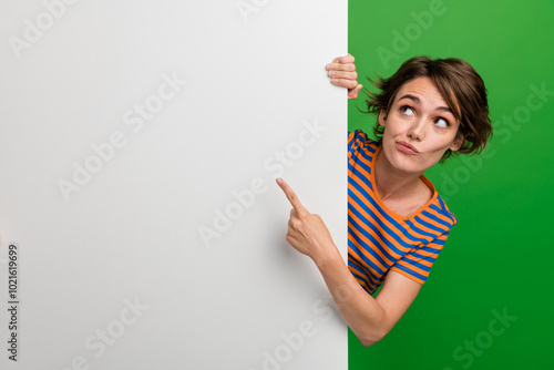 Photo portrait of pretty young girl finger point look white wall empty space wear trendy striped outfit isolated on green color background