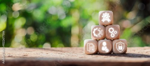 Wooden blocks with icons representing ISO 27001 information security management concepts on a natural, blurred background.