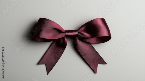 Elegant burgundy satin bow with long tails on a neutral gray background, showcasing detailed texture and sheen.