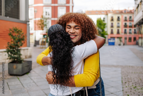 Trendy trans latin woman hugging friend in city street. Friends meeting, gen z lifestyle.