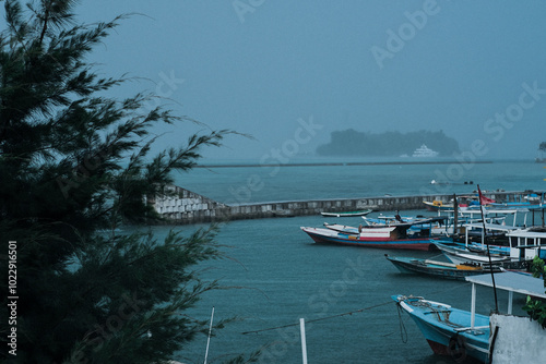 Moody beach landscape with rain falling over calm waters. A solitary boat rests by the shore, creating a serene and reflective atmosphere. The cloudy sky and soft waves evoke a sense of peace and soli