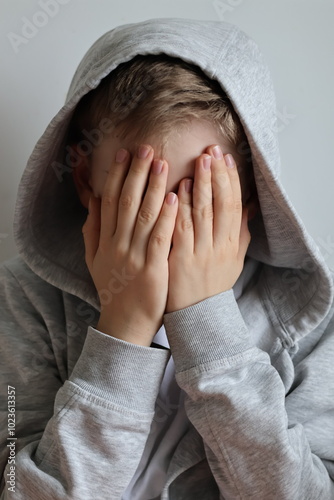 A sad, broken boy covering his face with his hands