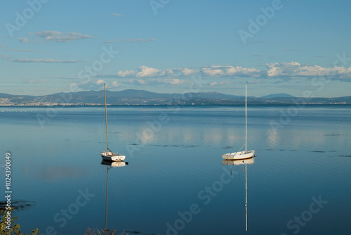 piccole barche a vela, ferme ed ormeggiate nell'acqua piatta e tranquilla del mare Adriatico, vicino a Trieste, con vista sulla costa lontana, durante un pomeriggio con cielo sereno in autunno