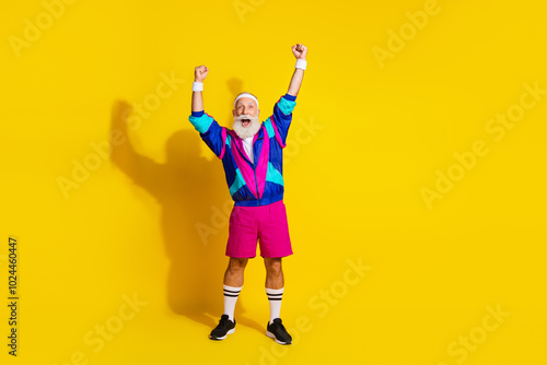 Full length photo of cheerful lucky mature guy dressed retro sport jacket rising fists emtpy space isolated yellow color background