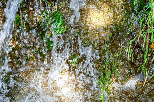 Splashes and bubbles in stream of clean fresh spring water in forest among branches, moss and grass.