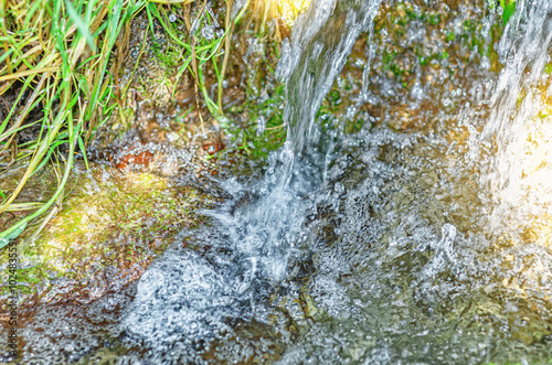 Splashes and bubbles in stream of clean fresh spring water in forest among branches, moss and grass.