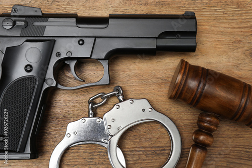 Gun, judge's gavel and handcuffs on wooden table, flat lay