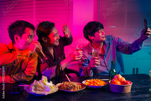 Three men are sitting at a table, holding glasses of beer and clinking glasses in celebration.They are enjoying food and drinks,eating and having fun in a party room with a happy,cheerful atmosphere