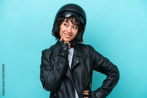 Young Argentinian woman with a motorcycle helmet isolated on blue background thinking an idea while looking up