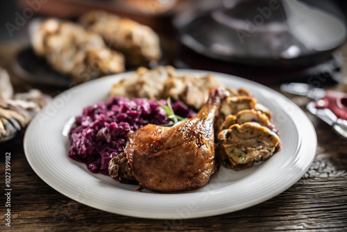 Portion of roast duck leg red cabbage homemade dumplings on plate and red wine on the background