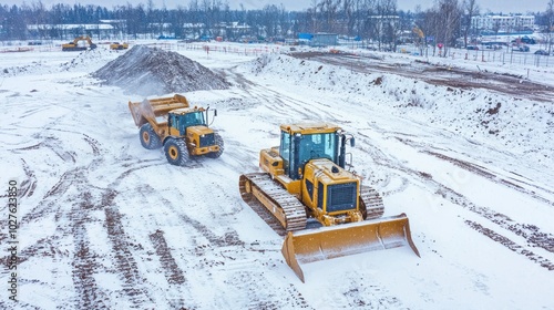 Bulldozers and trucks clearing snow at a construction site during winter.