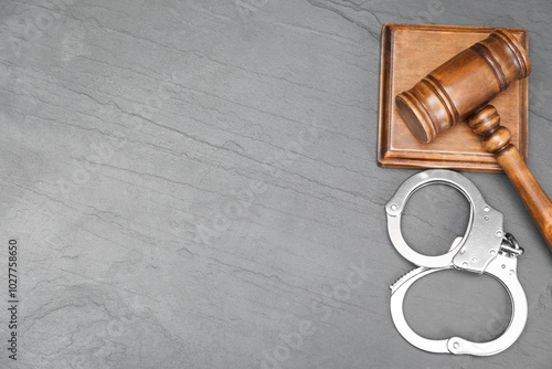 Judge's gavel and handcuffs on gray textured table, flat lay. Space for text