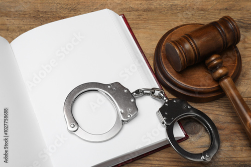 Book, judge's gavel and handcuffs on wooden table