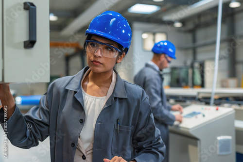 Two engineers, an Indian woman, and African American man, supervising the work of automatic machines at an industrial plant.