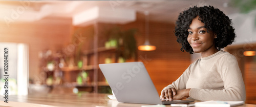 Smiling black lady using modern laptop at cafe, working online, empty space