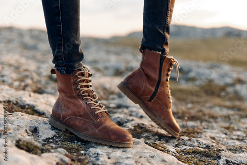 Golden hour glow woman in brown boots standing on rocky hill with sun setting behind her