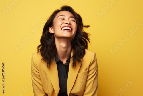 Portrait of a joyful asian woman in her 30s dressed in a stylish blazer over soft yellow background