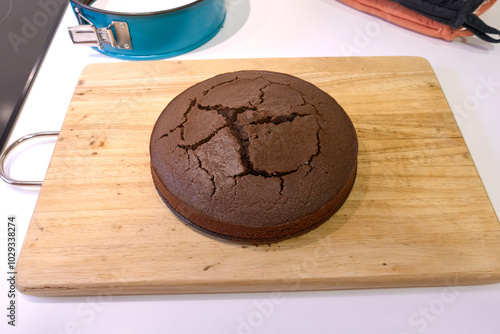 A freshly baked circle chocolate cake cracked placed on a wooden cutting board ready to be served