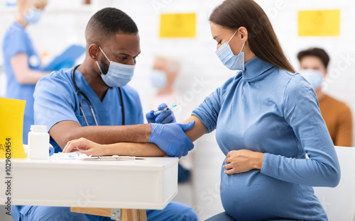 African American Doctor Giving Coronavirus Vaccine Injection Shot To Pregnant Woman, Wearing Protective Face Mask In Clinic Hospital. Corona Virus Vaccination, Patient Getting Vaccinated For Covid-19