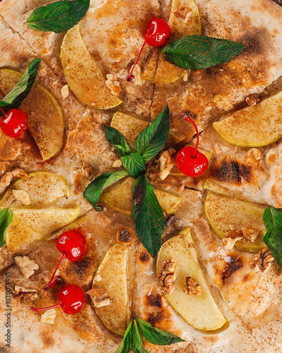 Delicious sweet pizza with apple slices, walnuts and cinnamon being decorated with mint and maraschino cherries