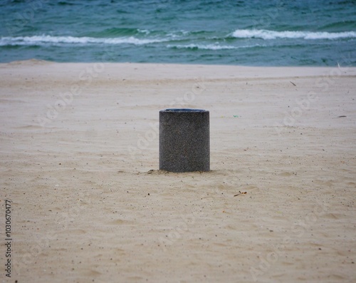 Kosz na śmieci na środku plaży. W tle fale na morzu.