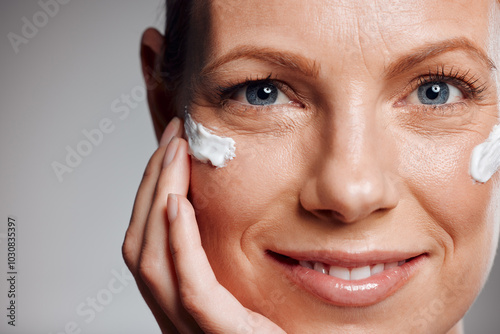 Portrait, mature woman and skincare cream for hydration, beauty or closeup. Lotion, happy model or hand apply cosmetics on face for dermatology, shine or glow for anti aging on gray studio background