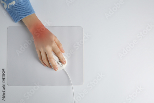 Woman suffering from pain in wrist while using computer mouse at white table, top view. Office work, Carpal tunnel syndrome