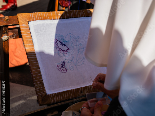 close-up shot of a woman from behind embroidering a flower on a white framed canvas