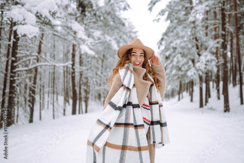 Happy woman among snowy trees in winter forest, enjoying the first snow in hat and coat. Boho style. Active lifestyle and tourism.