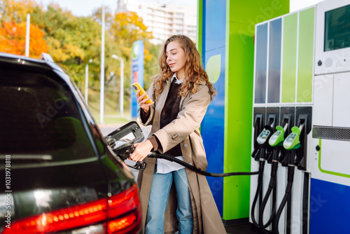 Beautiful woman filling her car with gasoline at the gas station. Online pay. Woman pays for a gas station using an app on her phone.