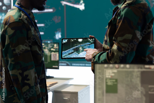 Team of diverse troopers examining satellite CCTV footage on a tablet, collecting information for a reconnaissance mission in command center. Soldiers engineers operating high tech gear.