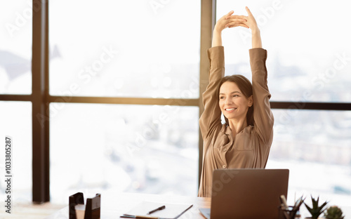 Smiling Young Woman In Brown Long Sleeve Shirt Stretching In Front Of Desk At Office, Looking Aside, Free Space