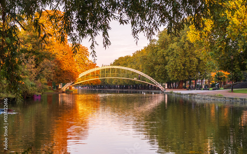 Sunrise lighting up the autumn foliage on the trees and Suspension Bridge over the River Great Ouse on the Embankment in Bedford, England