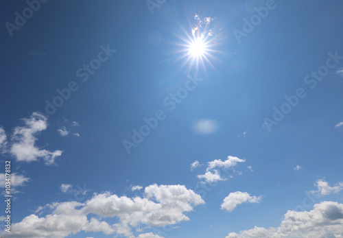 sun high in the blue sky with white clouds and you can see the sun's rays