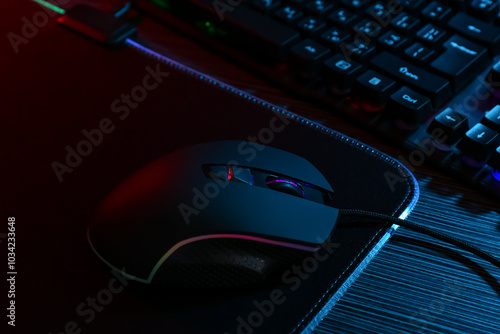 Computer mouse, mousepad and keyboard on dark wooden table in neon lights, closeup