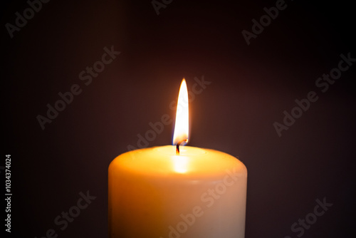 A single candle flame illuminating darkness in a serene indoor setting during evening hours. Baccground for funeral, obituary, in memoriam with copy space