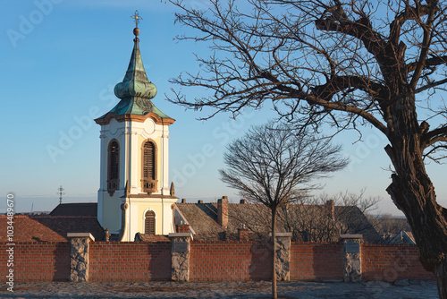 Blagovestenska Church tower rising above brick wall in late afternoon sun in Szentendre